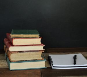 pile of books beside white printer paper and black ballpoint pen