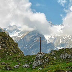 a cross on a grassy hill with mountains in the background
