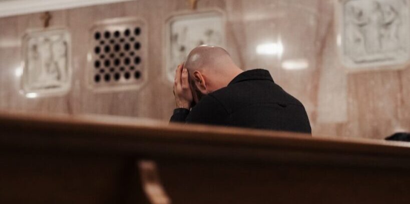 Man bowing head in prayer inside a church